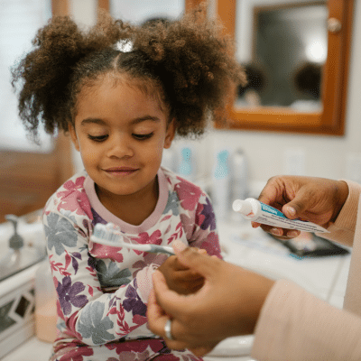 Little girl with pigtails preparing to brush her teeth with her mom's help, representing early dental care