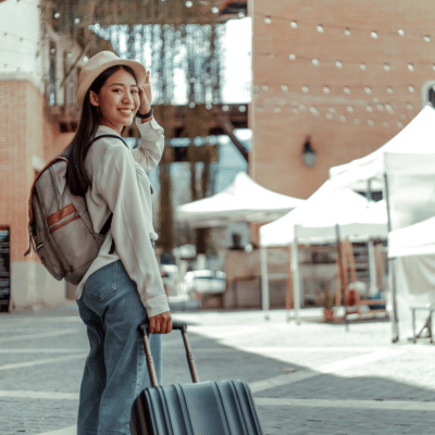 Woman wearing a white hat, backpack and pulling a suitcase, representing dental routine while traveling