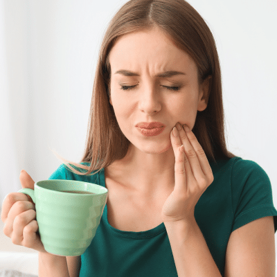 Woman holding a green cup and her jaw in pain, representing tooth sensitivity